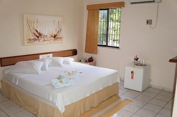 A neatly made bed with white linens and a small bedside table with a red object on it. - Hotel Malibu (Fortaleza)