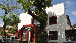 Un bâtiment moderne à la façade blanche et aux touches de couleur rouge, doté d’une entrée imposante avec une porte en verre et d’un petit balcon.