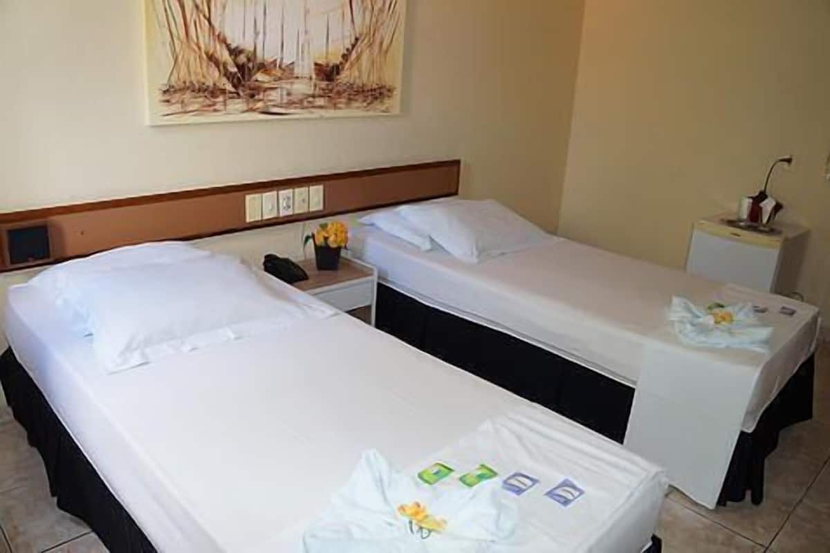 Une chambre d’hôtel avec deux lits simples, une table de chevet avec une lampe et un tableau au mur.