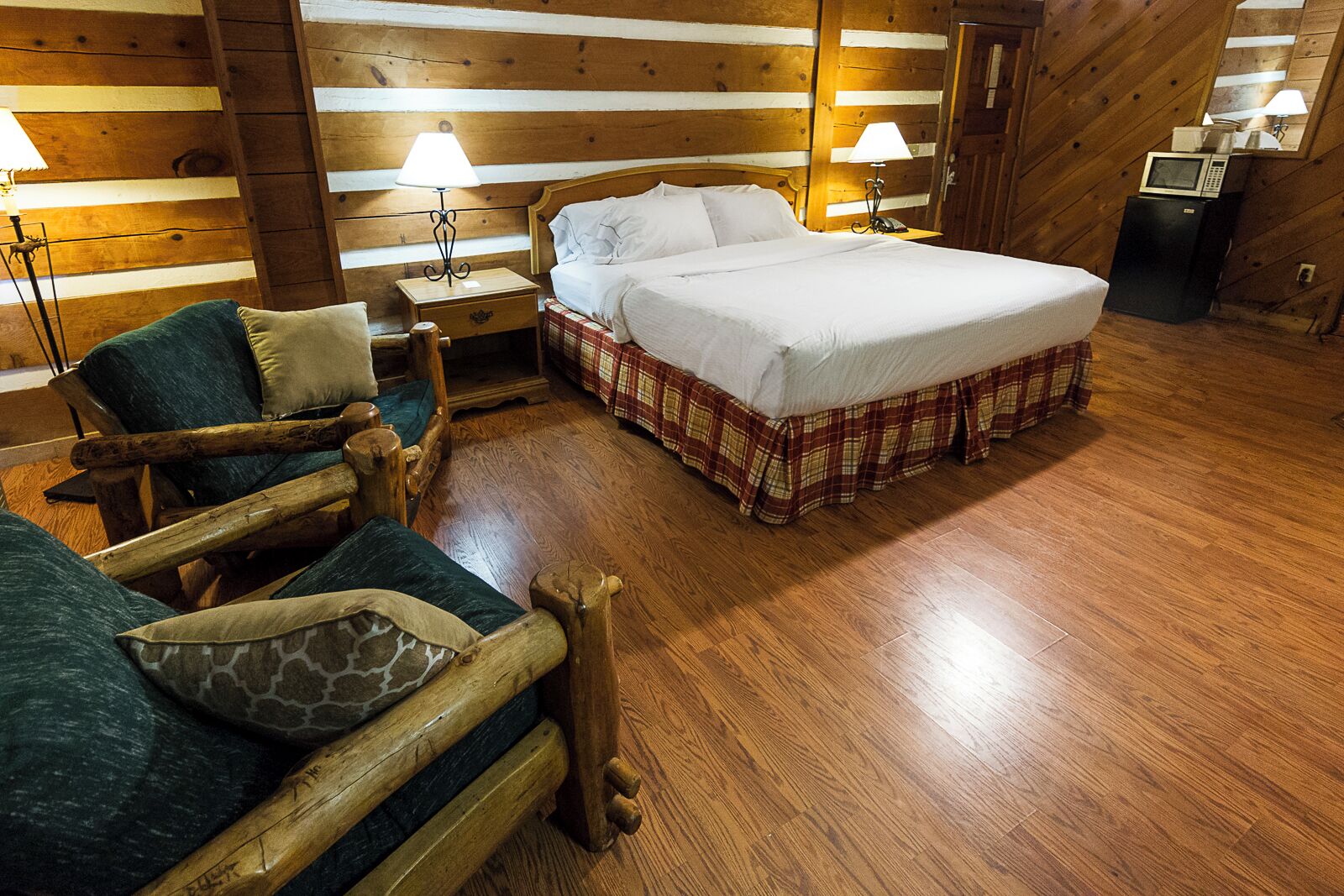 Ein Holzblockhaus-Innenraum mit einem Bett, zwei Stühlen, einem Nachttisch und einem kleinen Tisch.