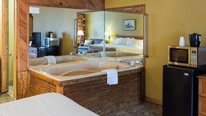 Habitación de hotel con una bañera grande, una cama, un espejo, un microondas y un refrigerador.