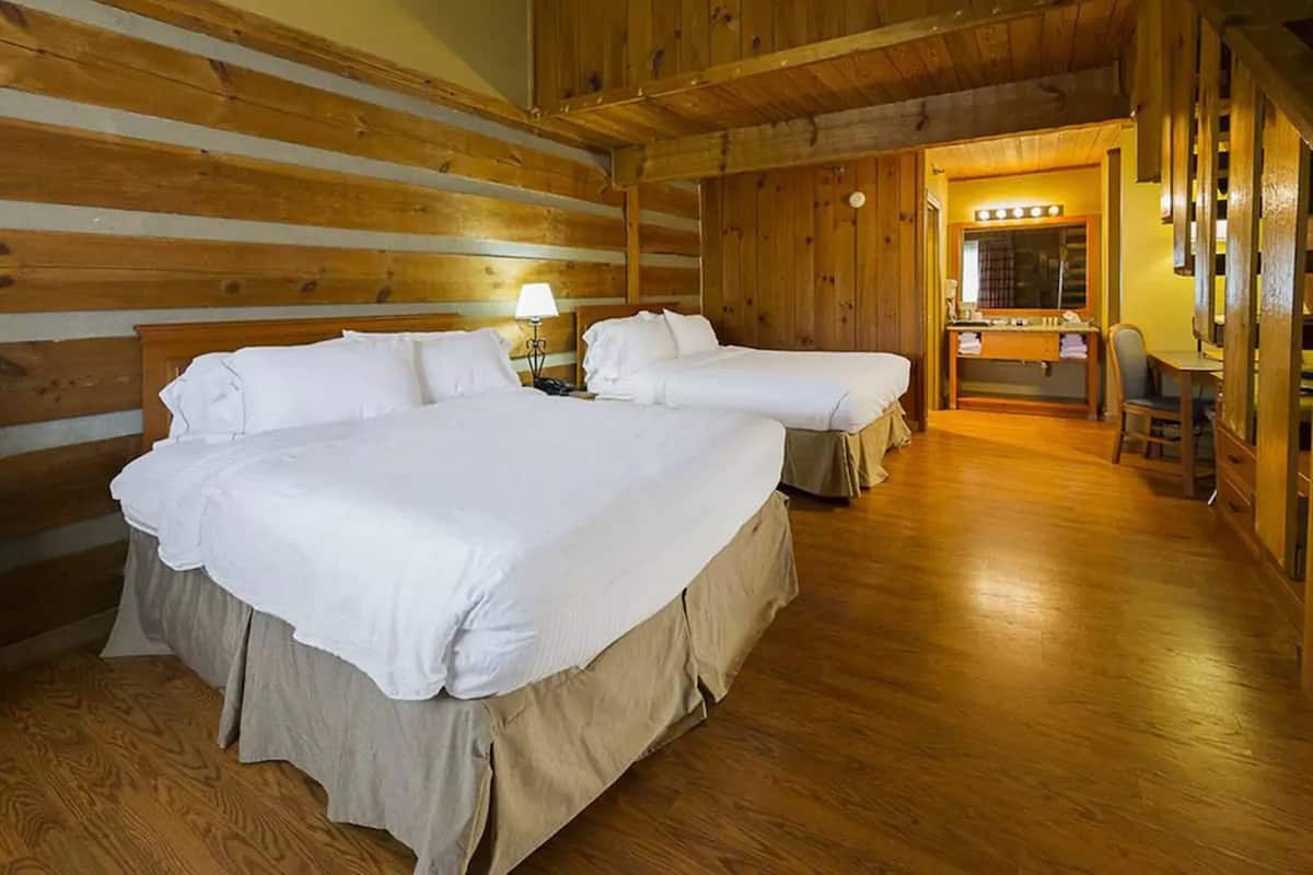 A log cabin-style room with two large beds, a wooden floor, a vanity with a mirror, and a small table with a chair.