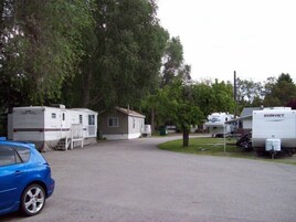 Un camping con vehículos recreativos y casas móviles, un camino pavimentado y un coche azul aparcado a la izquierda.