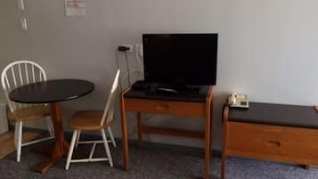 A small room with a wooden desk, a television, a chair, and a bed.