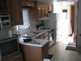 Una cocina compacta con armarios de madera, estufa, pileta y televisor.