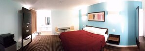 A hotel room with a bed, a desk, a chair, a TV, and a bathroom.