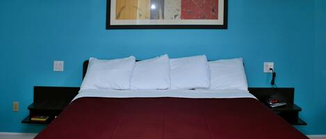 Une chambre d’hôtel avec un lit, une œuvre d’art encadrée au-dessus du lit et une table de chevet avec une télécommande.
