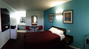 A hotel room with a bed, a desk with a chair, a TV, a mirror, and two framed pictures on the wall.