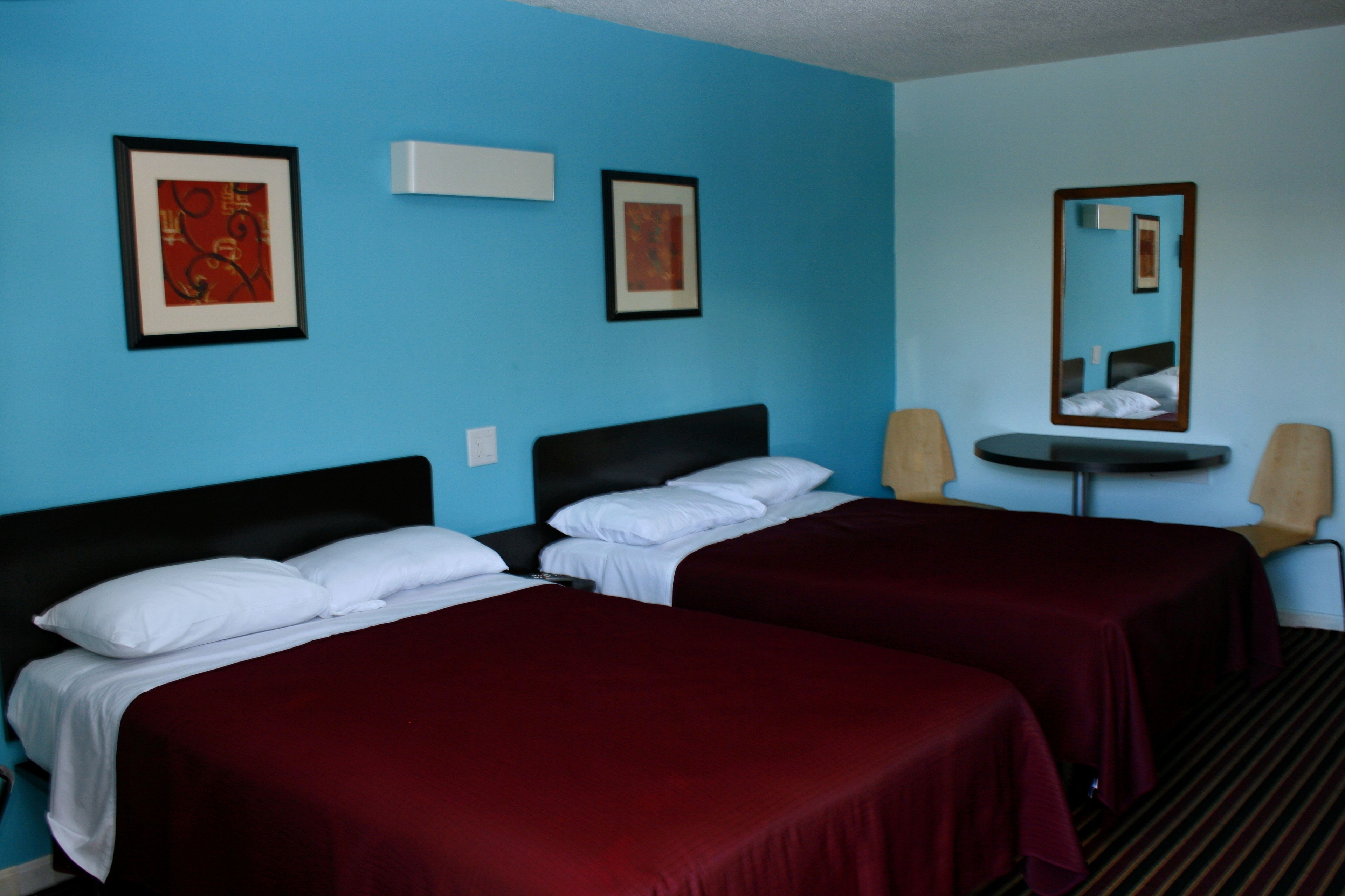 Una habitación de hotel con dos camas individuales, una mesita redonda pequeña, dos sillas y dos cuadros enmarcados en las paredes.