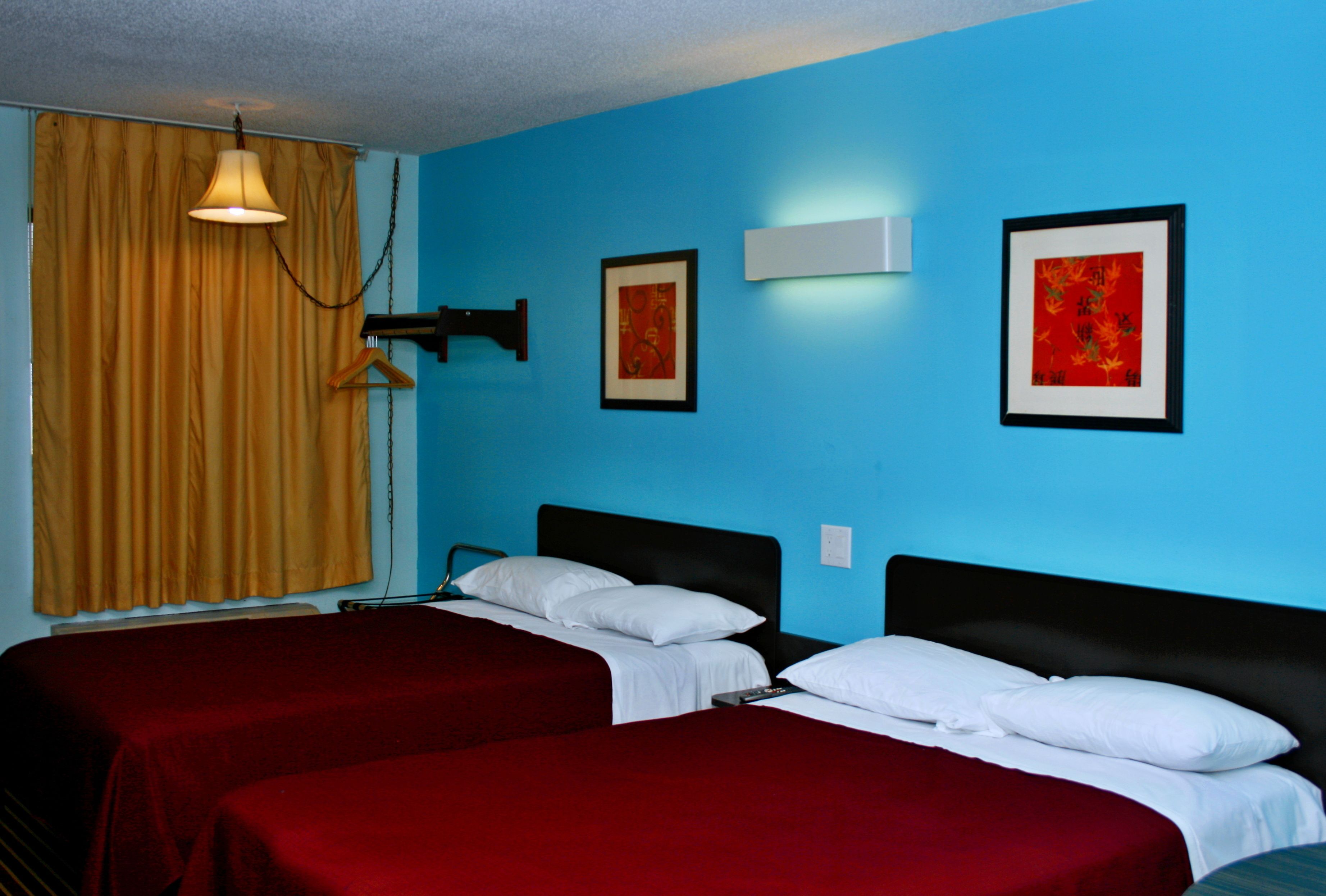 A room with two beds, a hanging light, and two framed pictures on the wall.