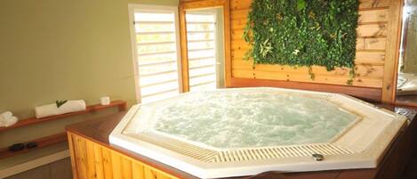 A wooden spa area with a hot tub, wooden shelves with towels, and a green wall with foliage.