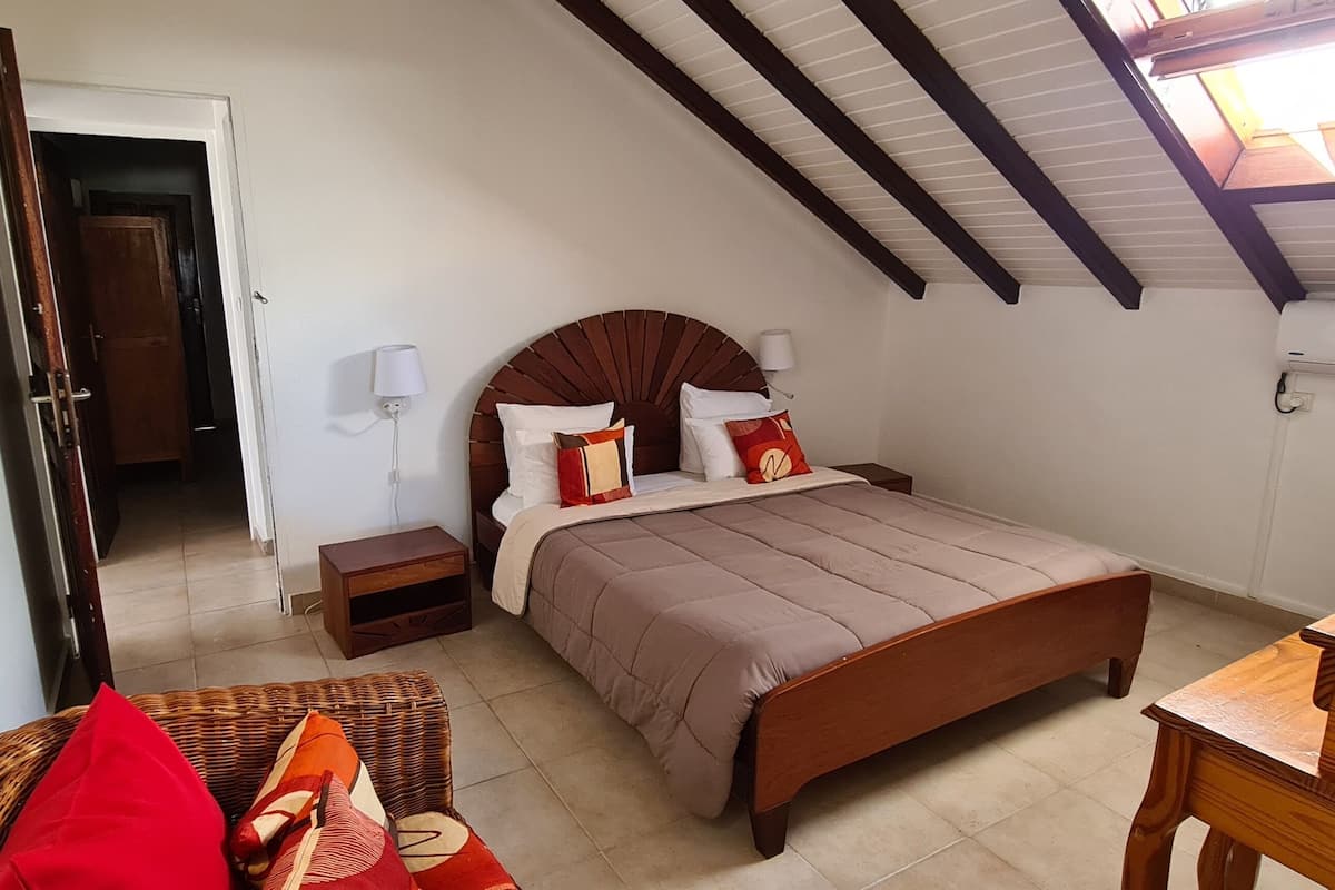 A bedroom with a sloped ceiling, a bed with a wooden headboard, a bedside table, a lamp, and a wooden dresser.