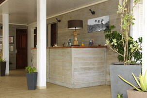 A reception area with a wooden reception desk, a lamp, a framed picture on the wall, and potted plants.