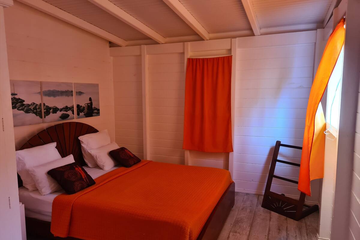 A bedroom with a bed, white walls, a wooden floor, and a painting of a landscape.