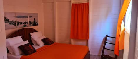 Une chambre à coucher avec un lit, des murs blancs, un plancher en bois et un tableau représentant un paysage.