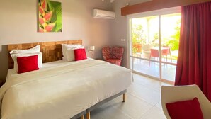 A bedroom with a large bed, a red chair, a ceiling fan, and a view of the outdoors. - Hotel Le Soleil Levant (Capesterre-de-Marie-Galante)