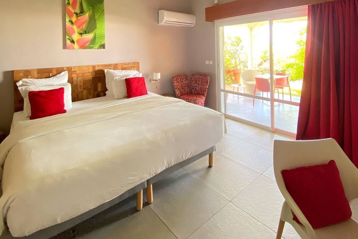 A bedroom with a large bed, a red chair, a ceiling fan, and a view of the outdoors.