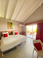 A bedroom with a large bed, a red chair, a ceiling fan, and a view of the outdoors.