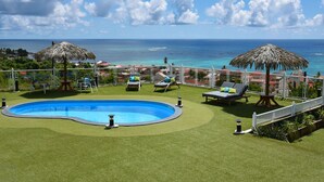 Zona de piscina con vista al océano, rodeada de sillones y sombrillas.