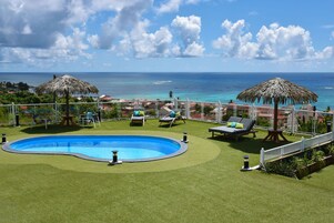A pool area with a view of the ocean, surrounded by lounge chairs and umbrellas.
