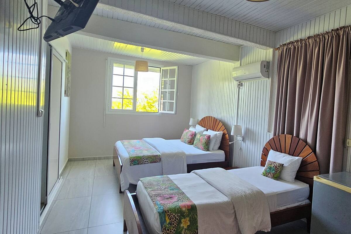 A room with two beds, a window with curtains, and an air conditioning unit.