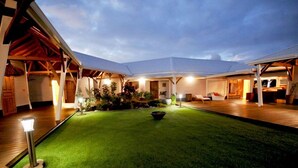A well-lit outdoor area with a green lawn, a seating area, and a covered section with a dining setup. - Hotel Le Soleil Levant (Capesterre-de-Marie-Galante)