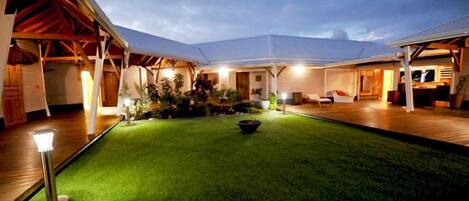 A well-lit outdoor area with a green lawn, a seating area, and a covered section with a dining setup.