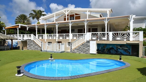 Una casa grande con piscina, terraza techada y un mural de tortugas marinas.