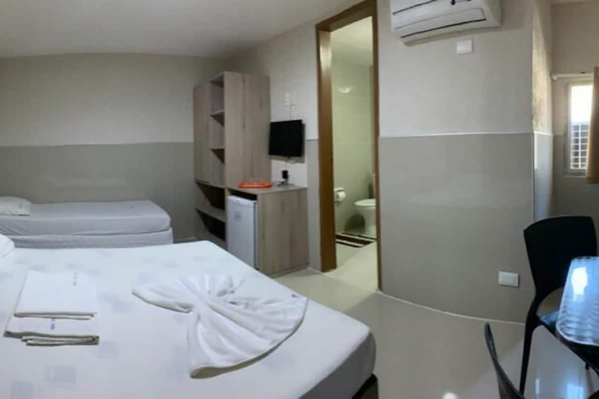 Ein Hotelzimmer mit zwei Betten, einem Schreibtisch, einem Stuhl und einem durchgehenden Türrahmen einsehbarer Badezimmer.