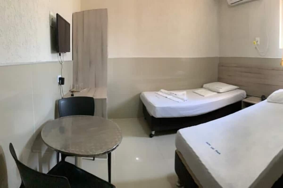 Ein kleines Hotelzimmer mit zwei Einzelbetten, einem runden Tisch, einem Stuhl, einem an der Wand befestigten Fernseher und einer Holzvertäfelung.