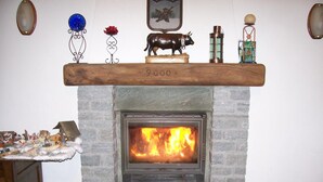 Ein Kamin aus Stein mit Feuer, eine darüberliegende Ablage mit Dekorationen und ein kleines Tischchen mit Figuren links.