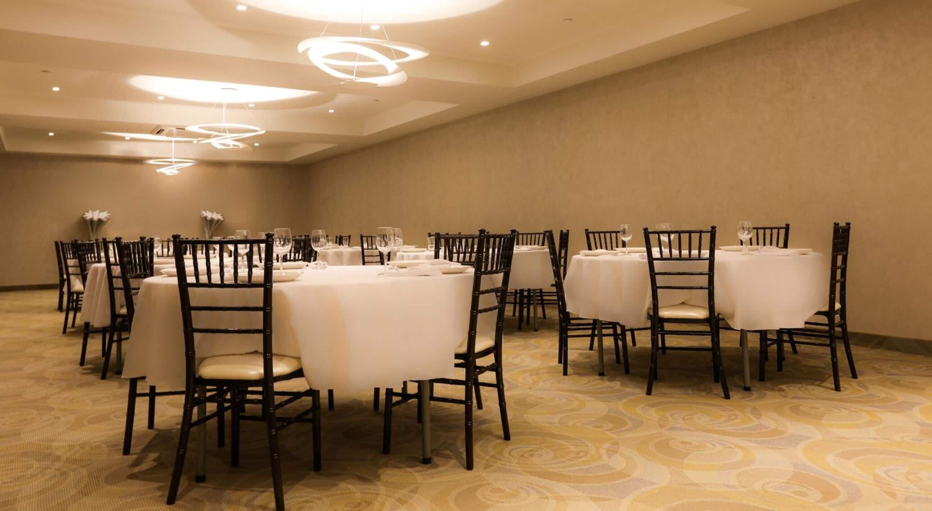 Un amplio salón de conferencias con mesas redondas, sillas negras y manteles blancos.