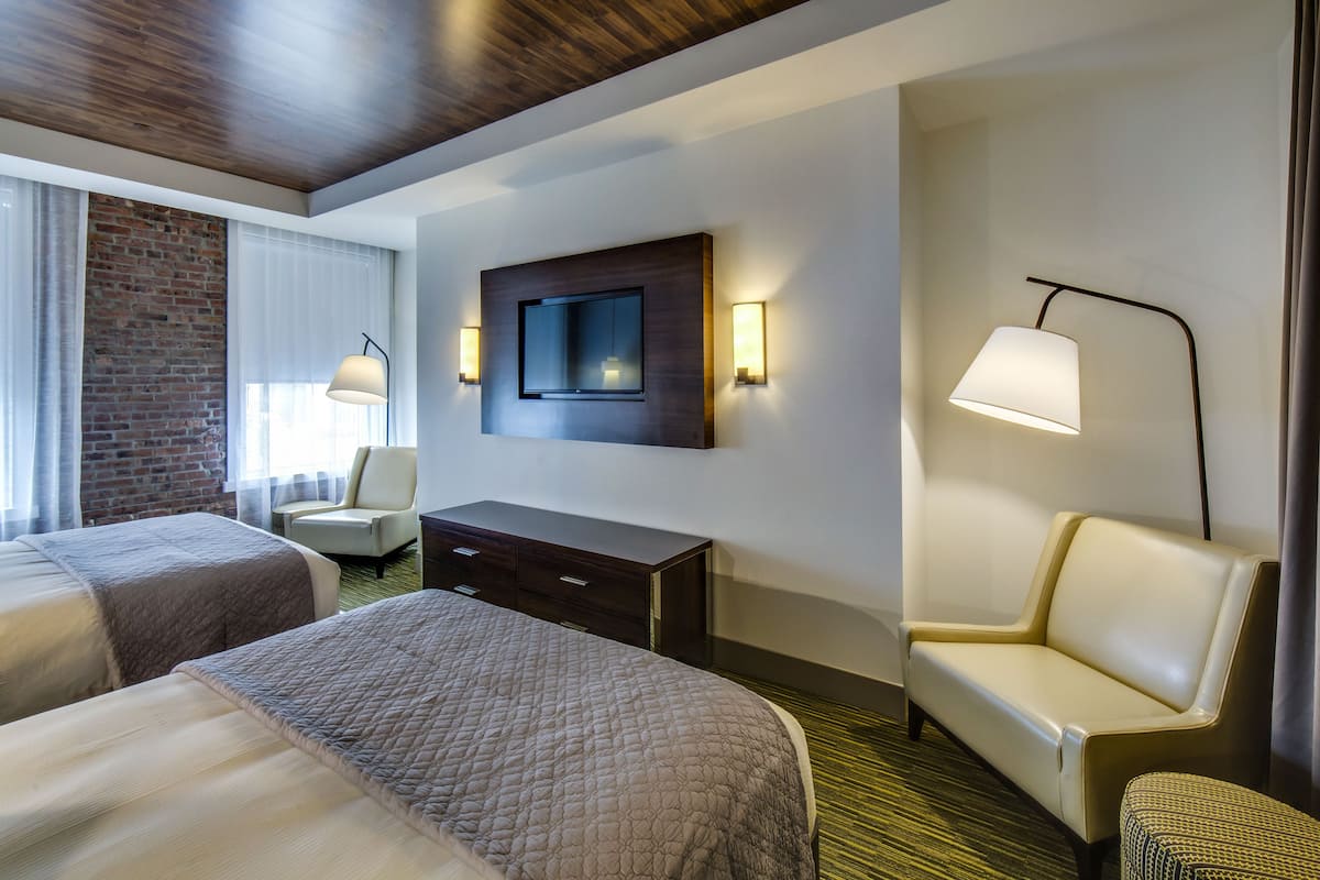 A hotel room with two beds, a TV mounted on the wall, a desk, a chair, and a sofa.