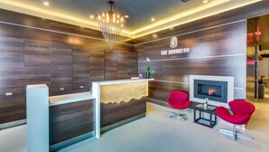 A modern hotel reception area with a wooden reception desk, a fireplace, and two red chairs. - The Brooklyn (Brooklyn)