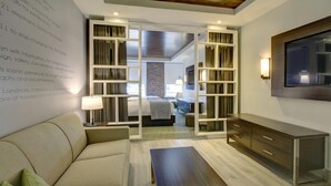 A modern hotel room with a sofa, a wooden table, a TV mounted on the wall, and a large window. - The Brooklyn (Brooklyn)