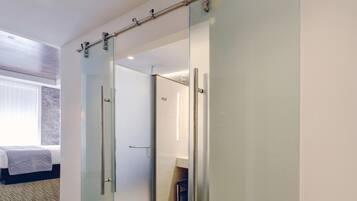 A hotel room with a sliding door leading to a bathroom, a bed with a white headboard, and a window with blinds.