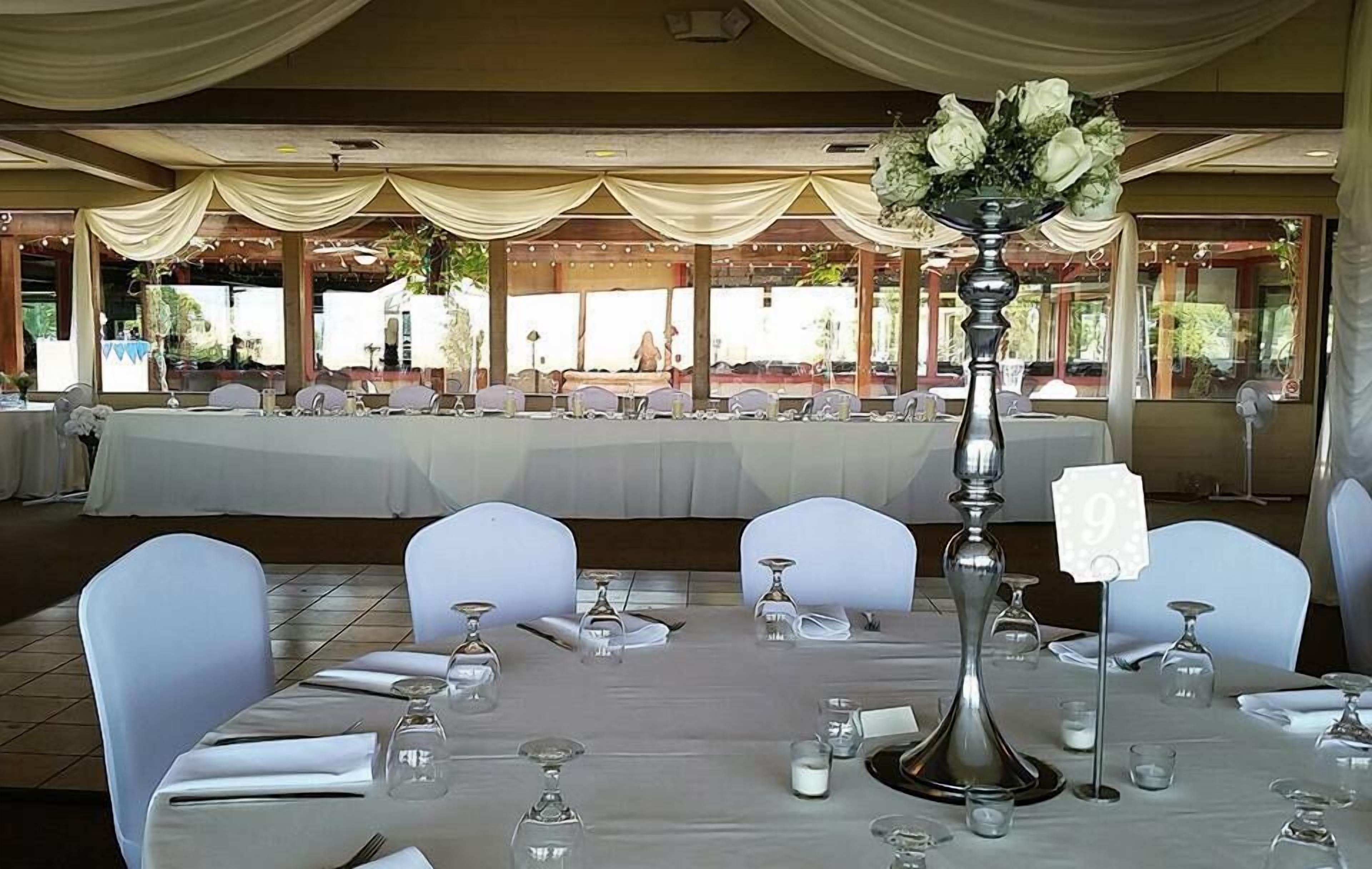 A banquet hall with white tablecloths, white chairs, and a central floral arrangement.