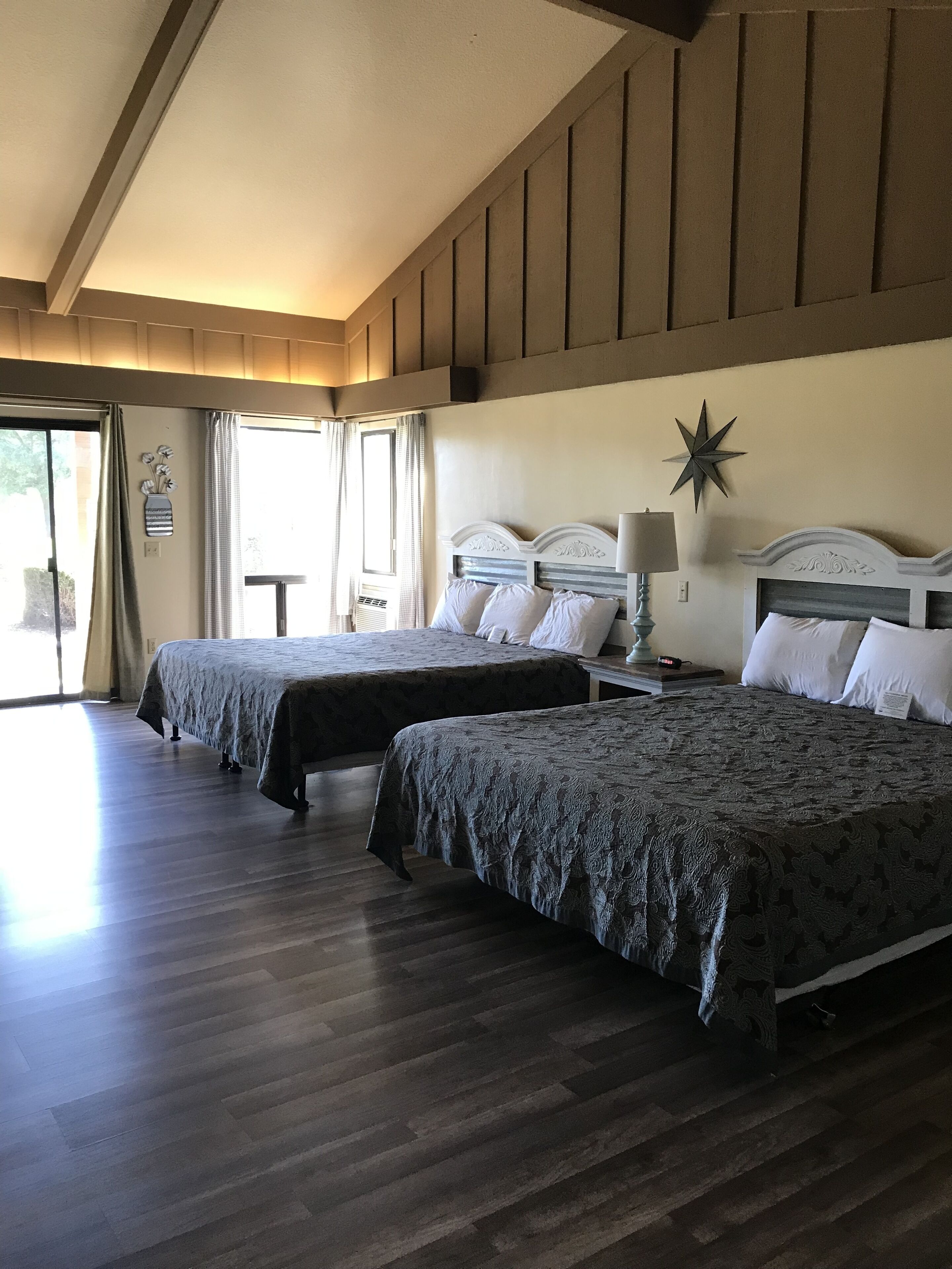 A hotel room with two beds, wooden flooring, a star decoration on the wall, and a window with curtains.