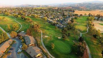 An aerial view of a residential area with houses, a golf course, and a parking lot.
