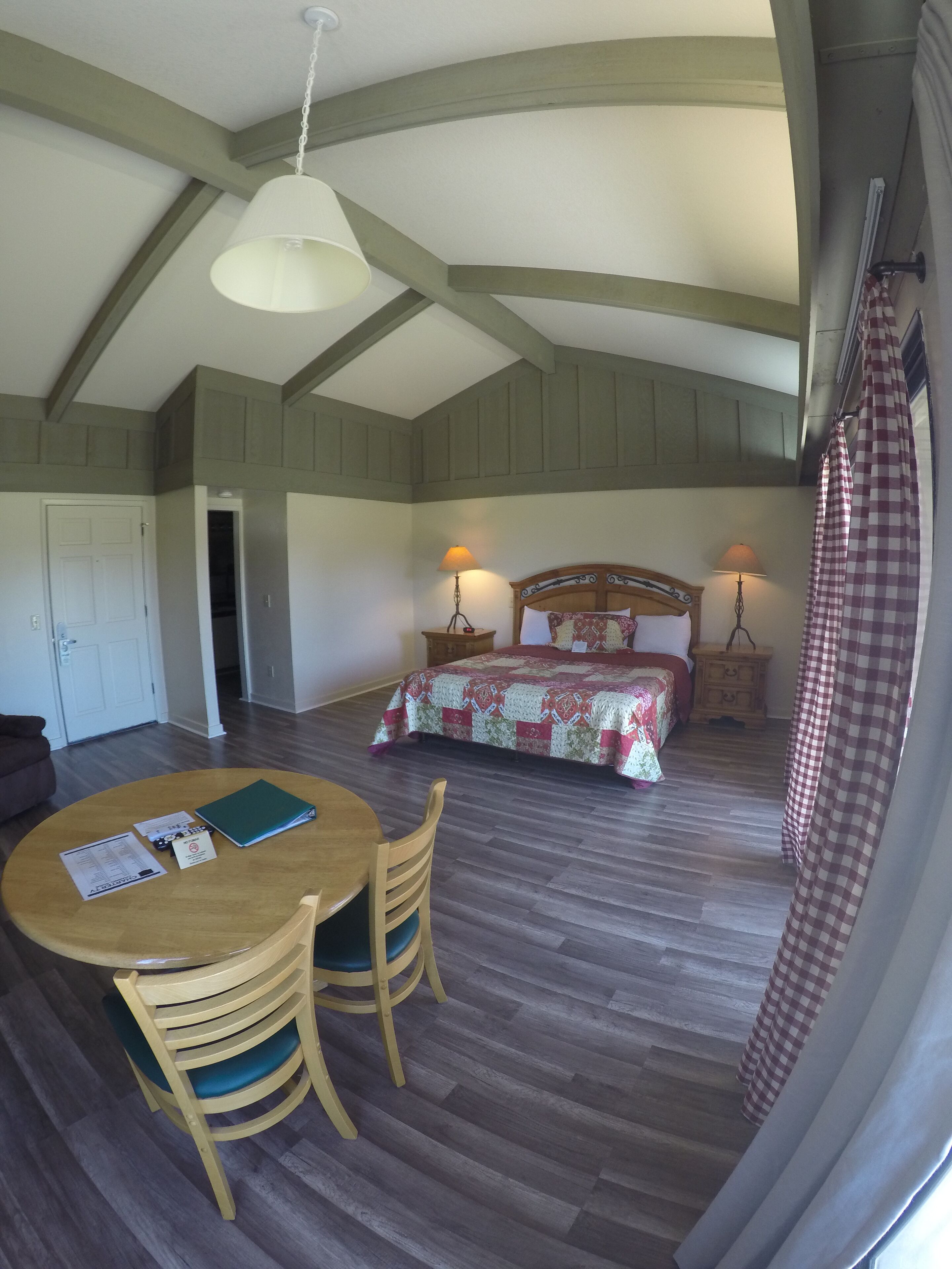 A bedroom with a large bed, two bedside lamps, a wooden headboard, and a checkered curtain.