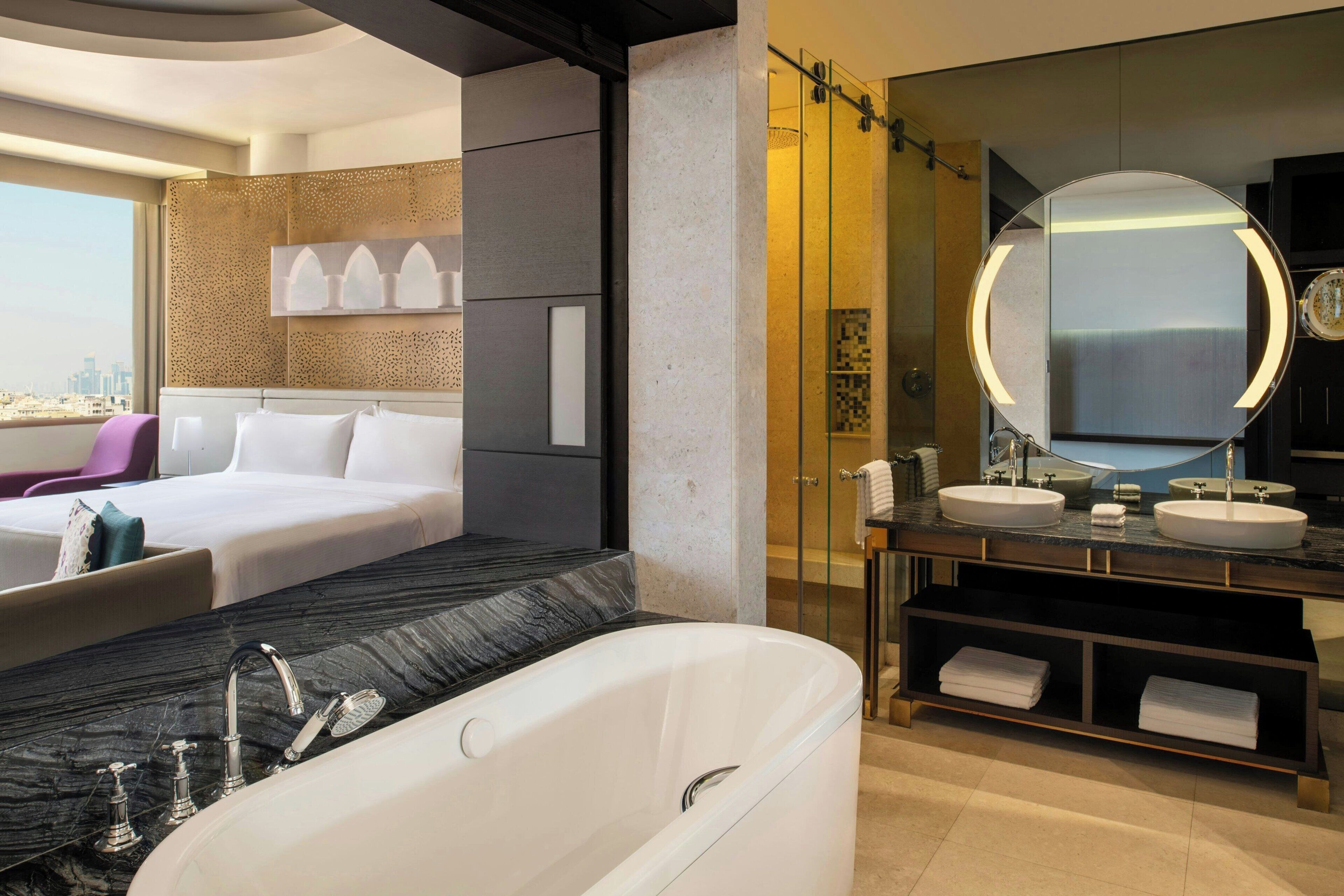 Ein modernes Hotelzimmer mit einem großen Bett, einem separaten Badezimmer mit Badewanne und Blick auf die Stadt.