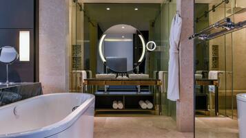 A modern bathroom with a large bathtub, dual sinks, a round mirror with lights, and a glass shower enclosure.