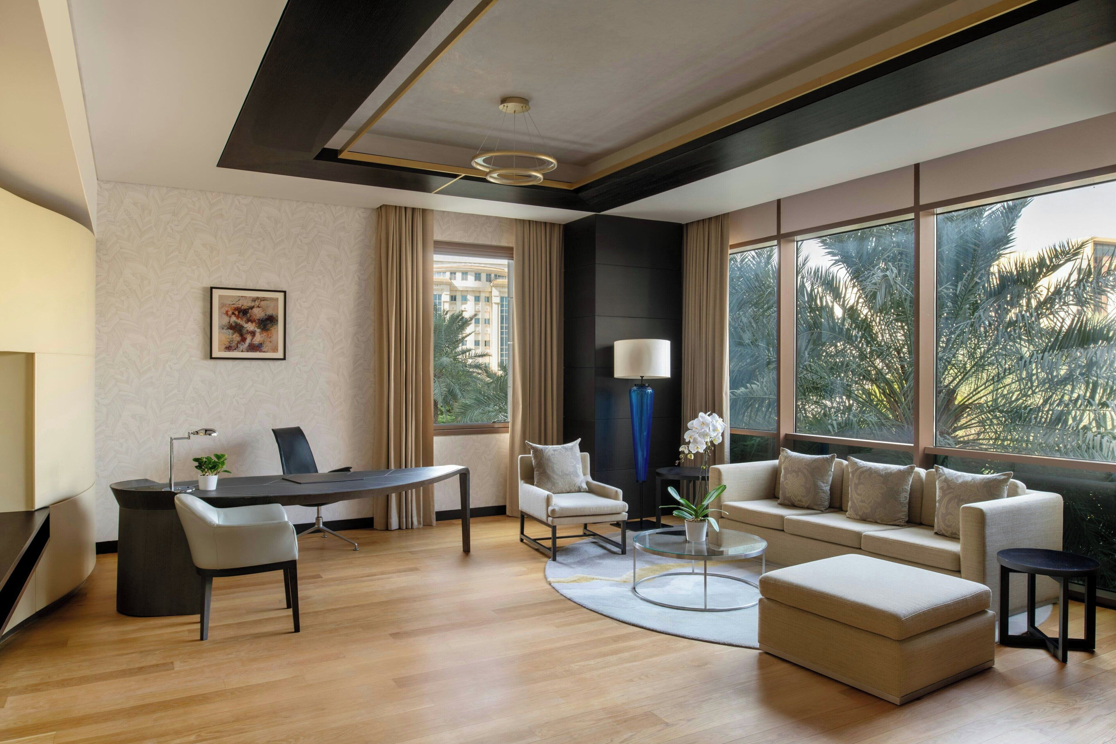 Una habitación de hotel moderna con un ventanal grande, un sofá, un escritorio y una mesa de centro.
