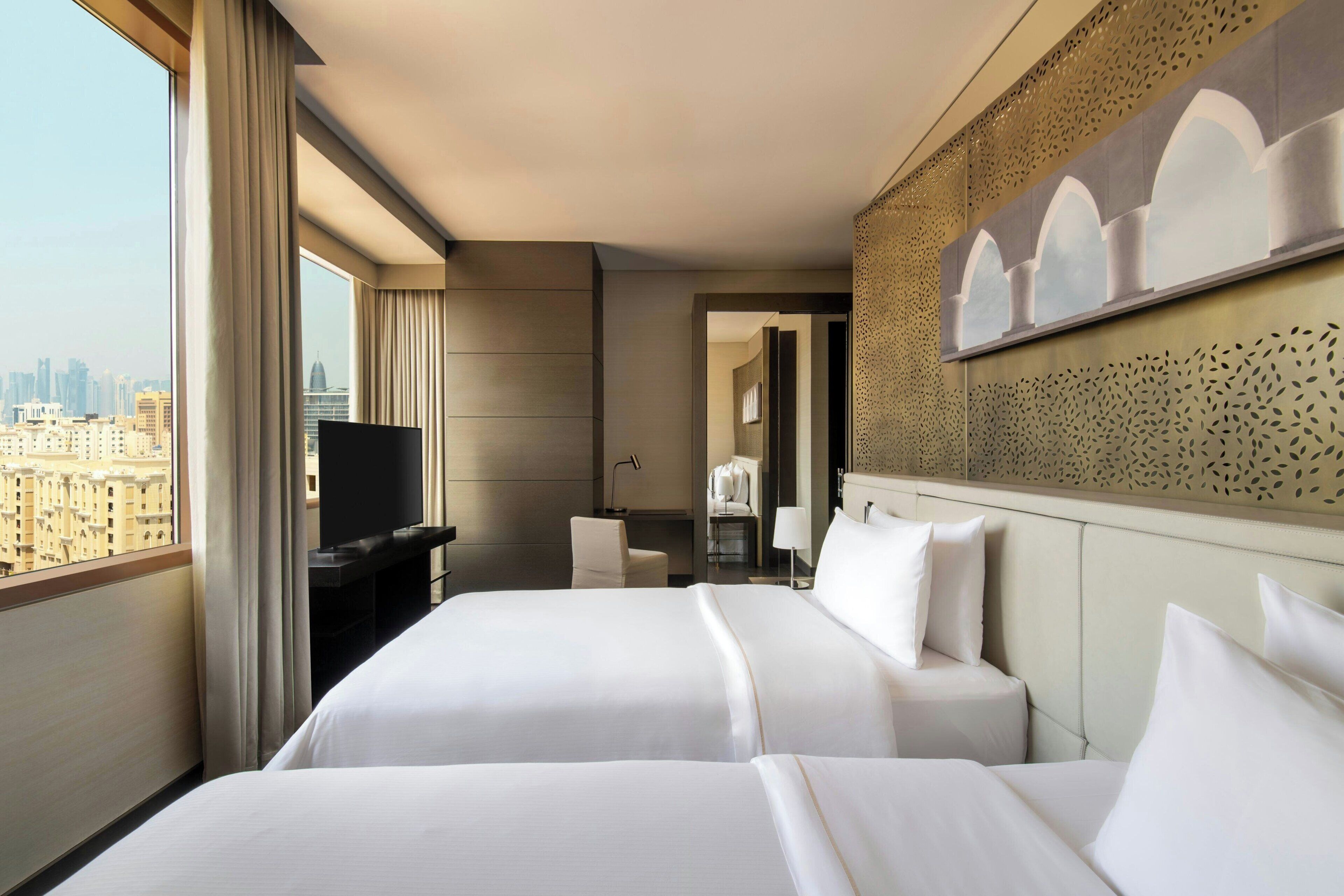 Ett hotellrum med två sängar, en TV och utsikt över staden.
