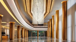 Un vestíbulo amplio con piso reflectante, grandes columnas doradas y un candelabro central.