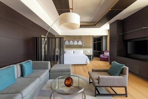 A modern hotel room with a sofa, armchair, and a glass coffee table. There is a bed with a white headboard and a TV mounted on the wall. - The Westin Doha Hotel & Spa (Doha)