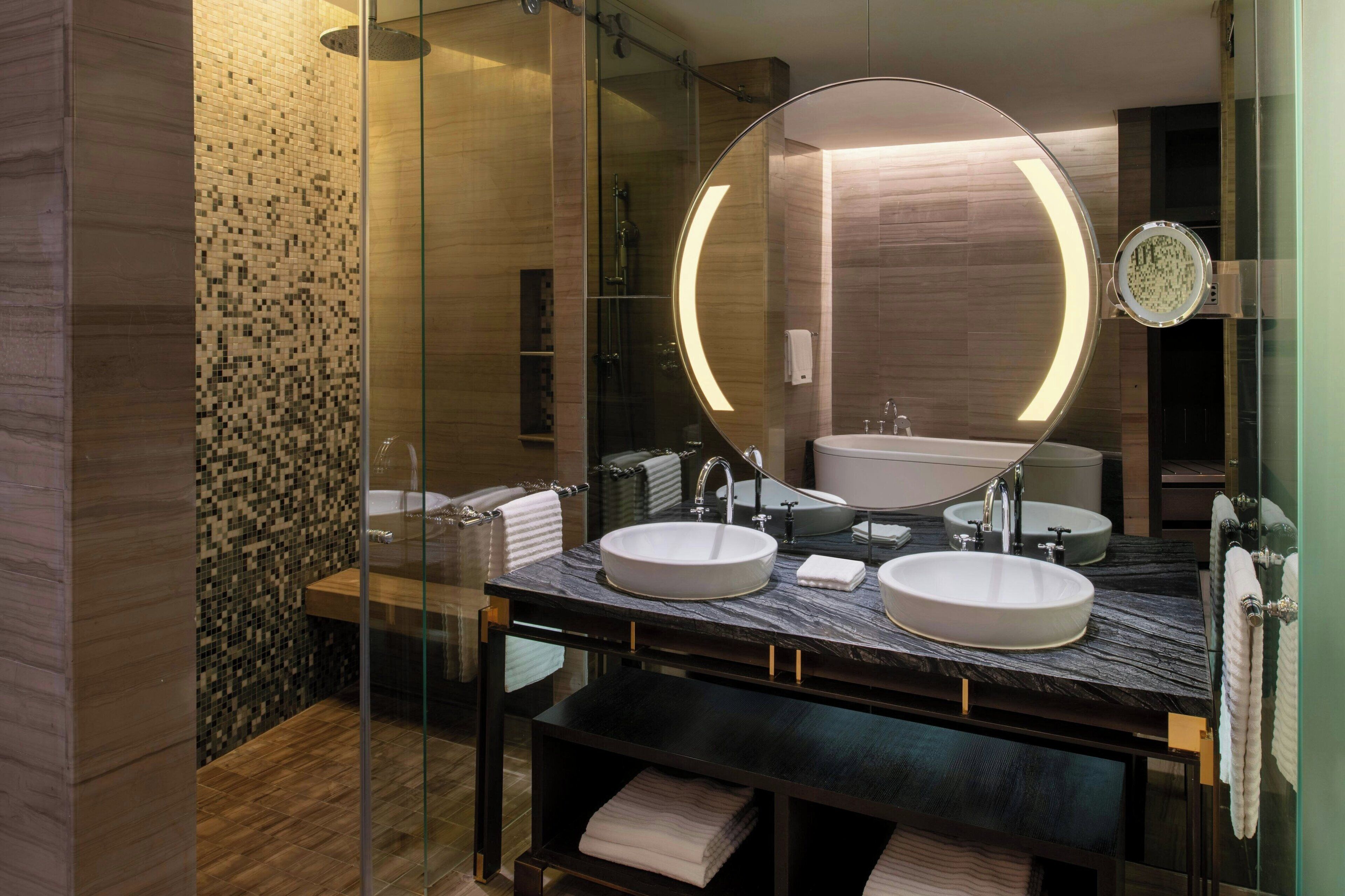 A modern bathroom with a large mirror, two sinks, and a glass shower enclosure.