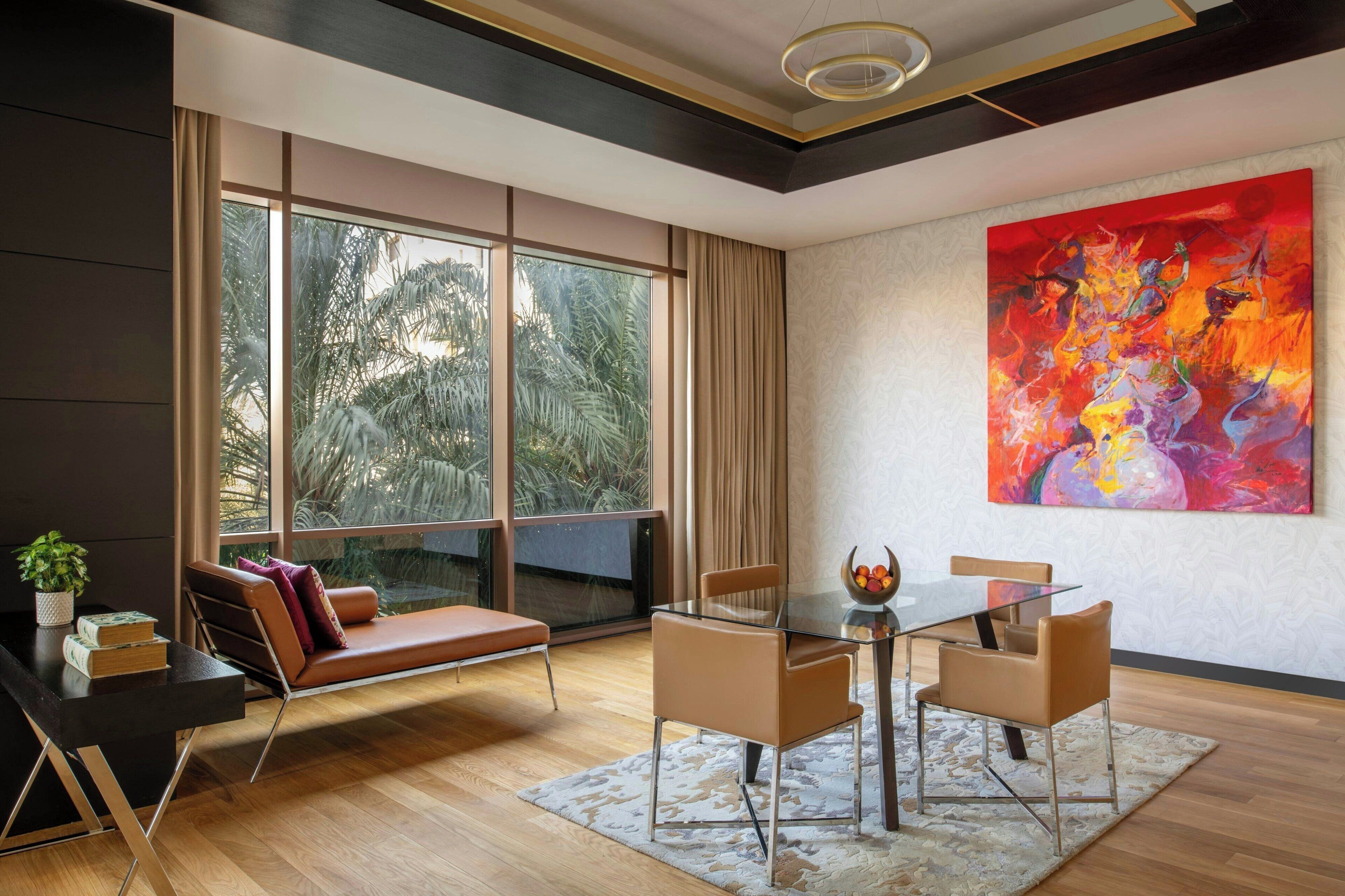 Una sala de estar moderna con una mesa de vidrio, sofá de cuero y amplias ventanas que ofrecen vista a palmeras.