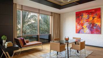 Una sala de estar moderna con una mesa de vidrio, sofá de cuero y amplias ventanas que ofrecen vista a palmeras.