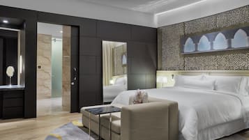 A modern hotel room with a large bed, a sitting area, a desk, and a bathroom visible through an open door.